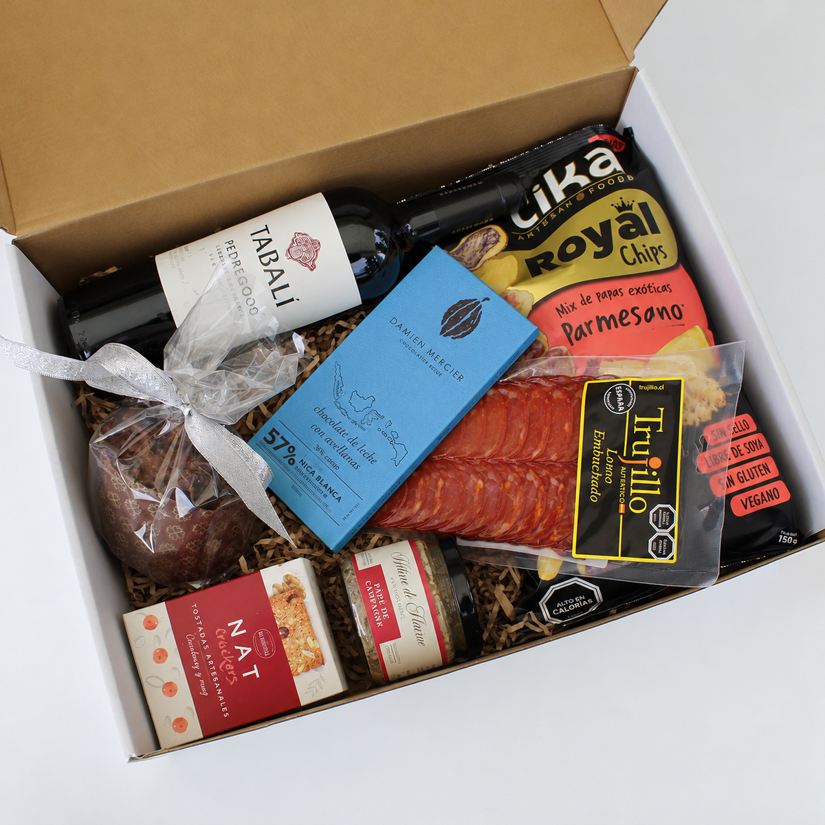 Regalo corporativo con vino Tabalí, Mousse o Paté de Foie Hélenè de Fleurac, lomo embuchado, chips Tika, galletas nat crackers, barra de chocolate Damien Mercier y pan de Pascua. Todo en una caja kraft natural, negra o blanca con cinta y tarjeta de saludo con logo corporativo.