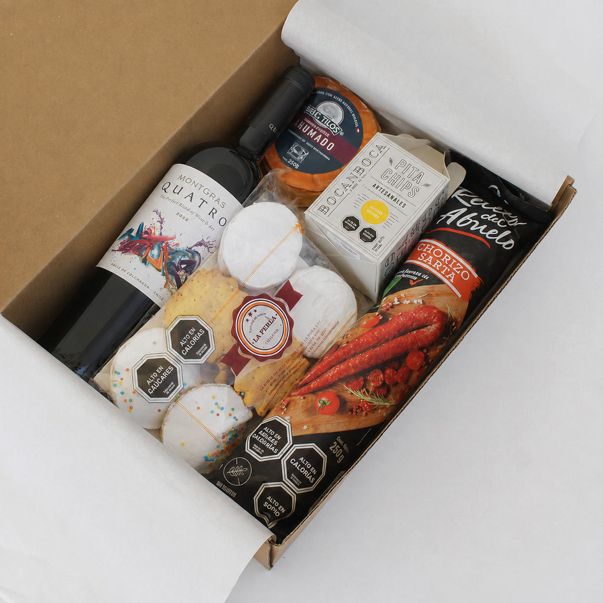 Caja gourmet con vino Quatro ensamblaje Viña Montgras, queso ahumado, chorizo artesanal, pita chips y dulces chilenos. Un regalo corporativo que celebra los sabores auténticos de Chile.