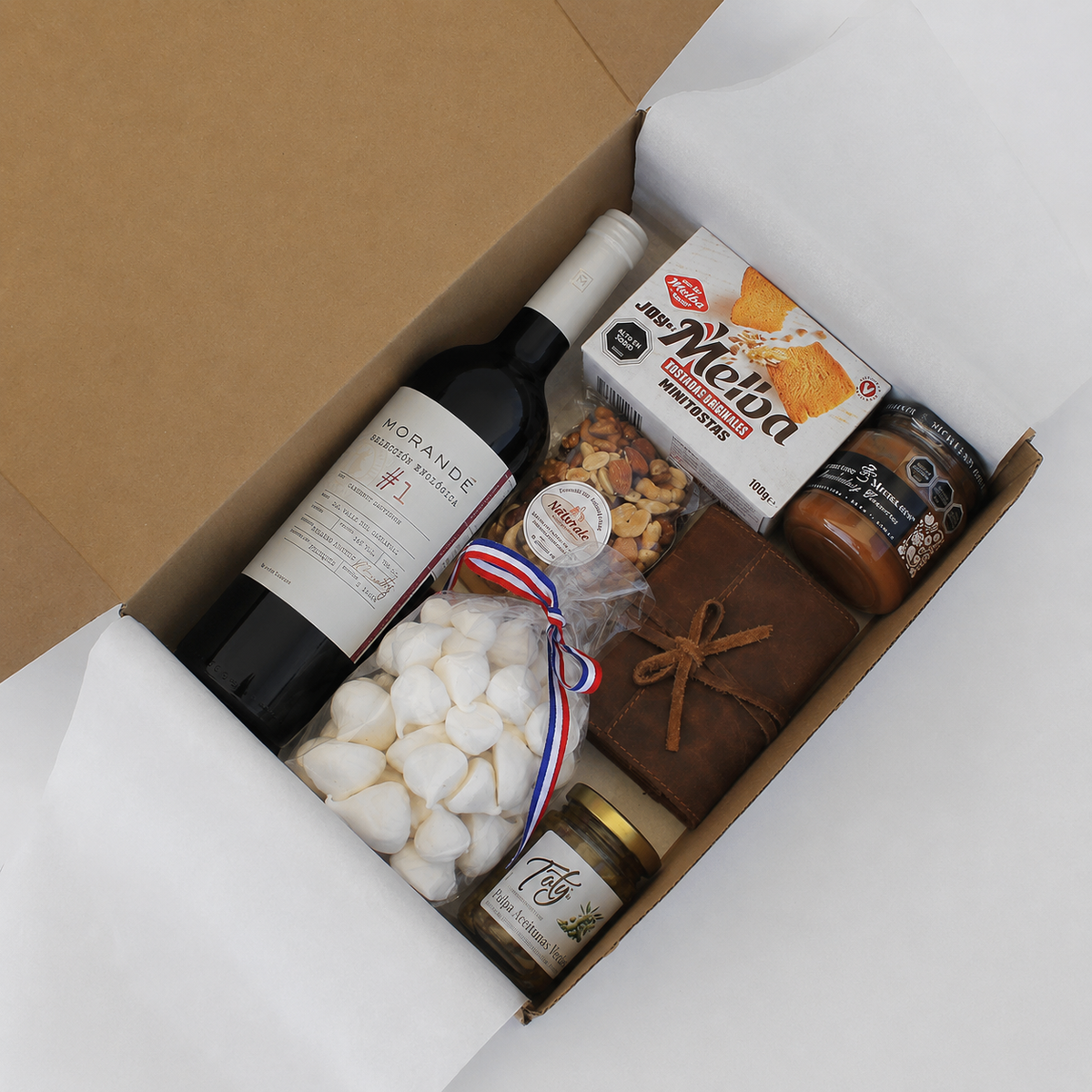Caja gourmet con Vino Morandé Selección enológica #1, juego de naipes en estuche de cuero, dulces, frutos secos y productos gourmet. Un regalo corporativo ideal para compartir y disfrutar momentos memorables.
