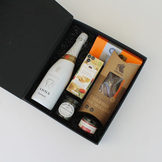 Regalo corporativo con Anna Codorniu, charqui de wagyu, chutney, turrón de Alicante, gourmet Hélène de Fleurac y crackers. Presentación en caja forrada negra con tapa imantada y cinta.