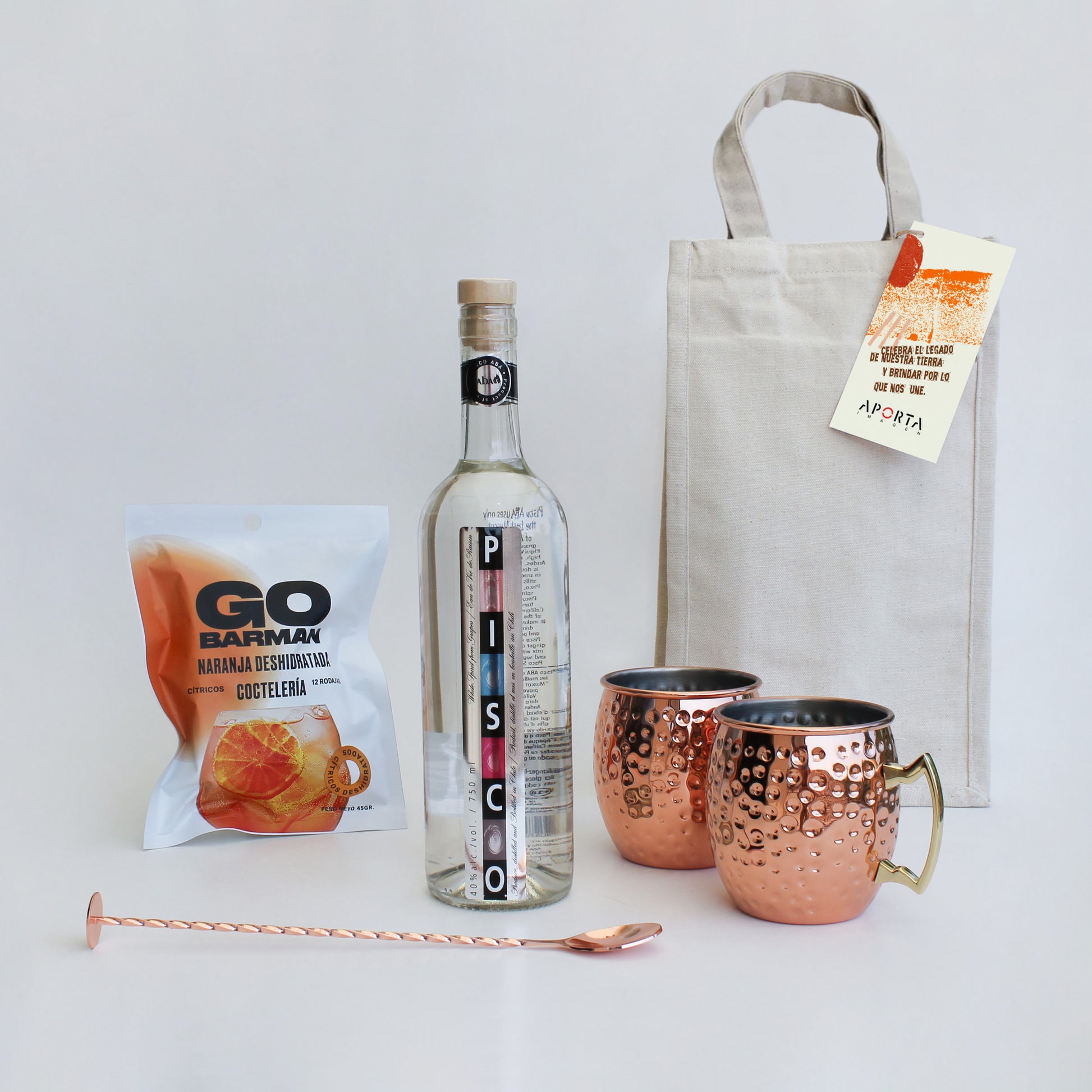 Pisco Aba 750cc, 2 mug cobre 500cc, cucharilla y naranja deshidratada Go Barman. En bolsa de algodón con tarjeta personalizada.