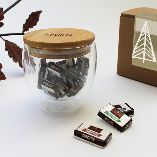 Un detalle de calidez y diseño. Taza de doble vidrio (250ml) con tapa de bambú y 15 mini chocolates alemanes Sarotti. El regalo corporativo ideal para momentos de bienestar. ¡Personalízalo con tu logo y sorprende con exclusividad!